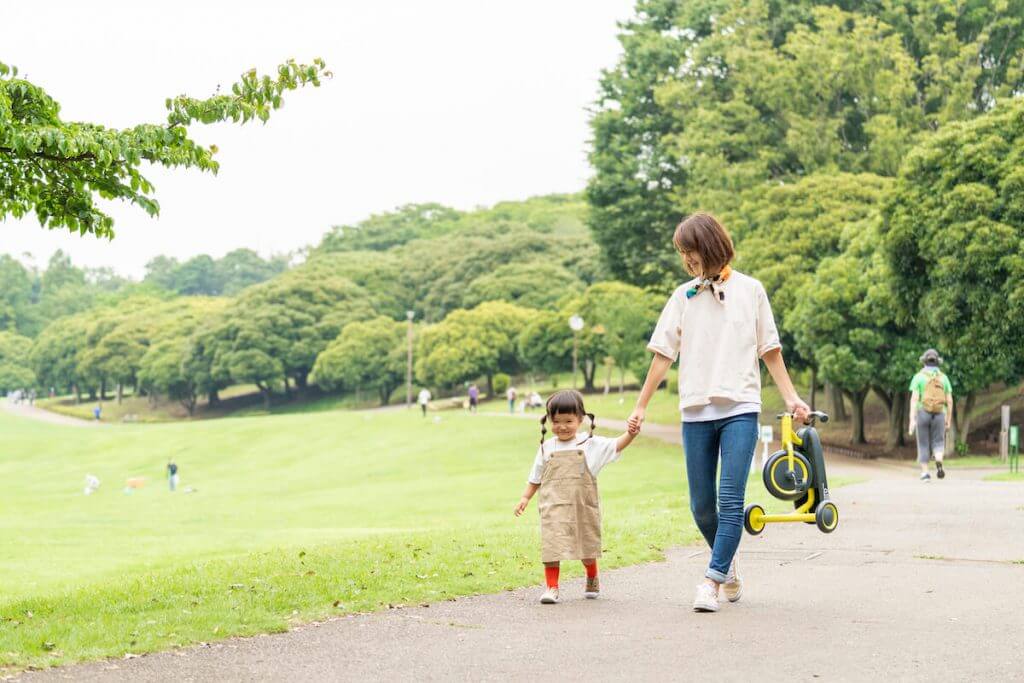 女の子が三輪車を持っているお母さんと歩いている様子