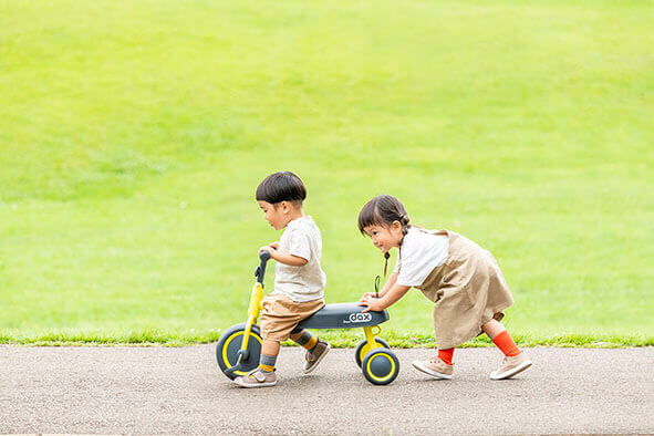 男の子を女の子が三輪車で遊んでいる様子