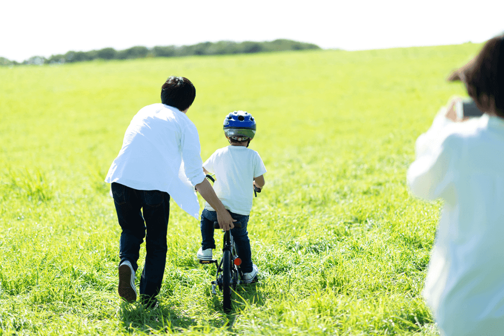 自転車デビューに挑戦する男の子とサポートするパパと見守るママ