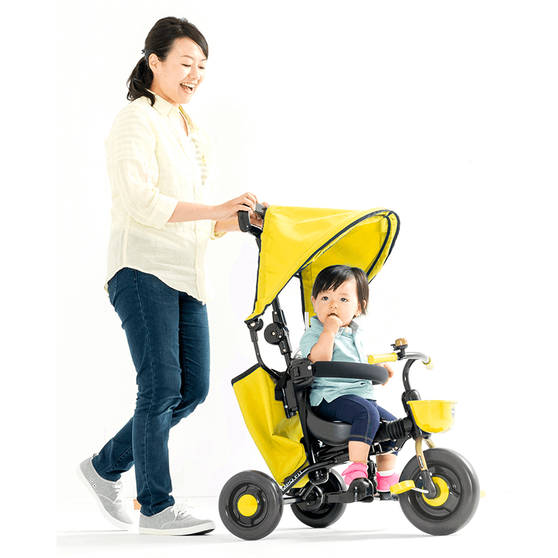 黄色のコントロールバーつき三輪車にのる女の子とママ